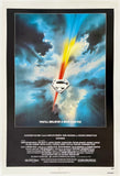A vintage Superman movie poster with a black border, featuring a dramatic sky scene with blue and white clouds, a bright yellow and red beam of light, and the Superman shield logo in the center. The bottom section contains white text credits on a black background.